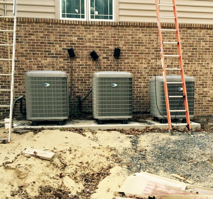Three air conditioners are lined up in front of a brick wall