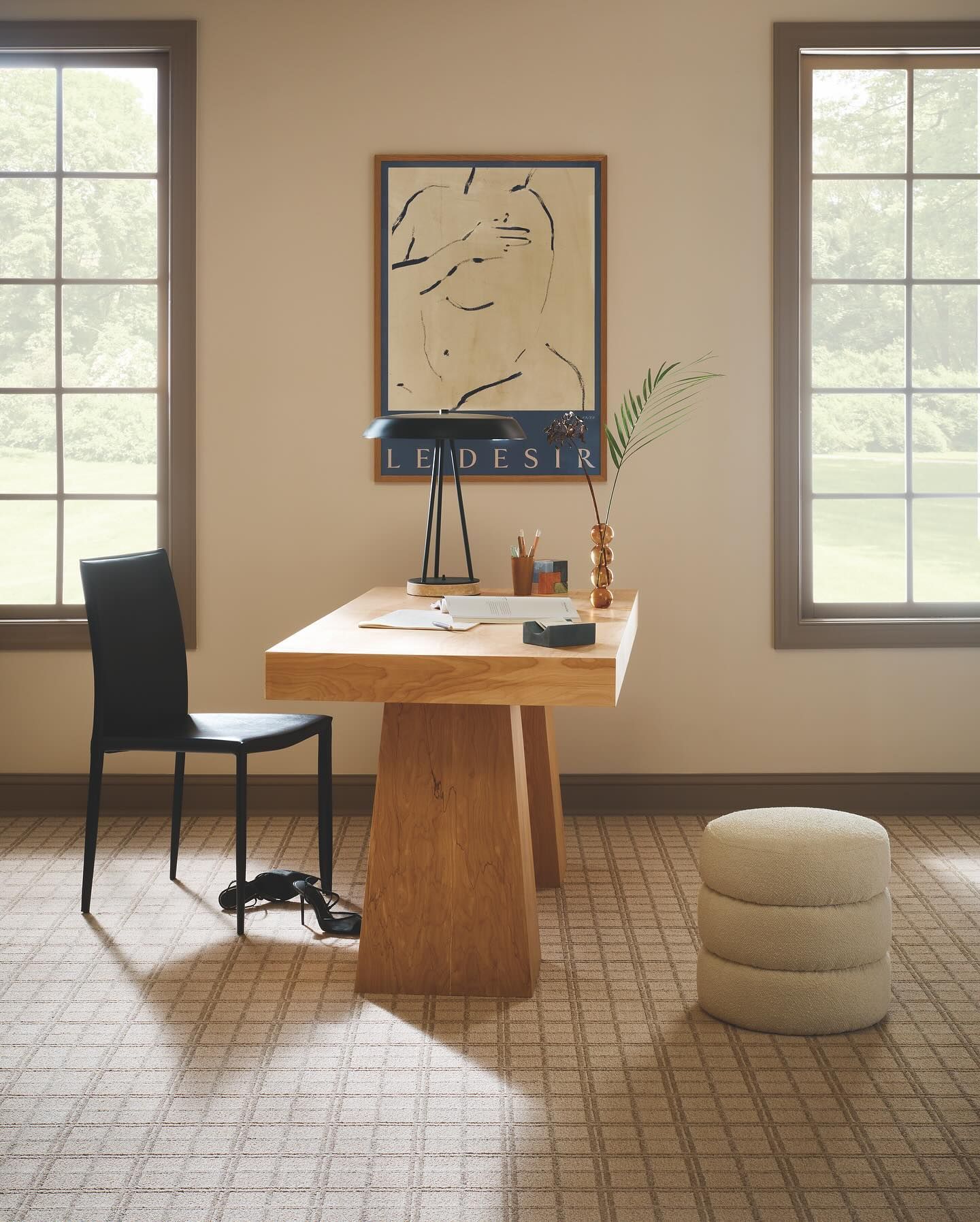 A room with a desk, chair, ottoman and a painting on the wall.