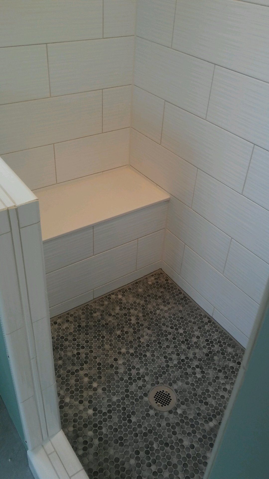 A shower with a bench and a drain in it.