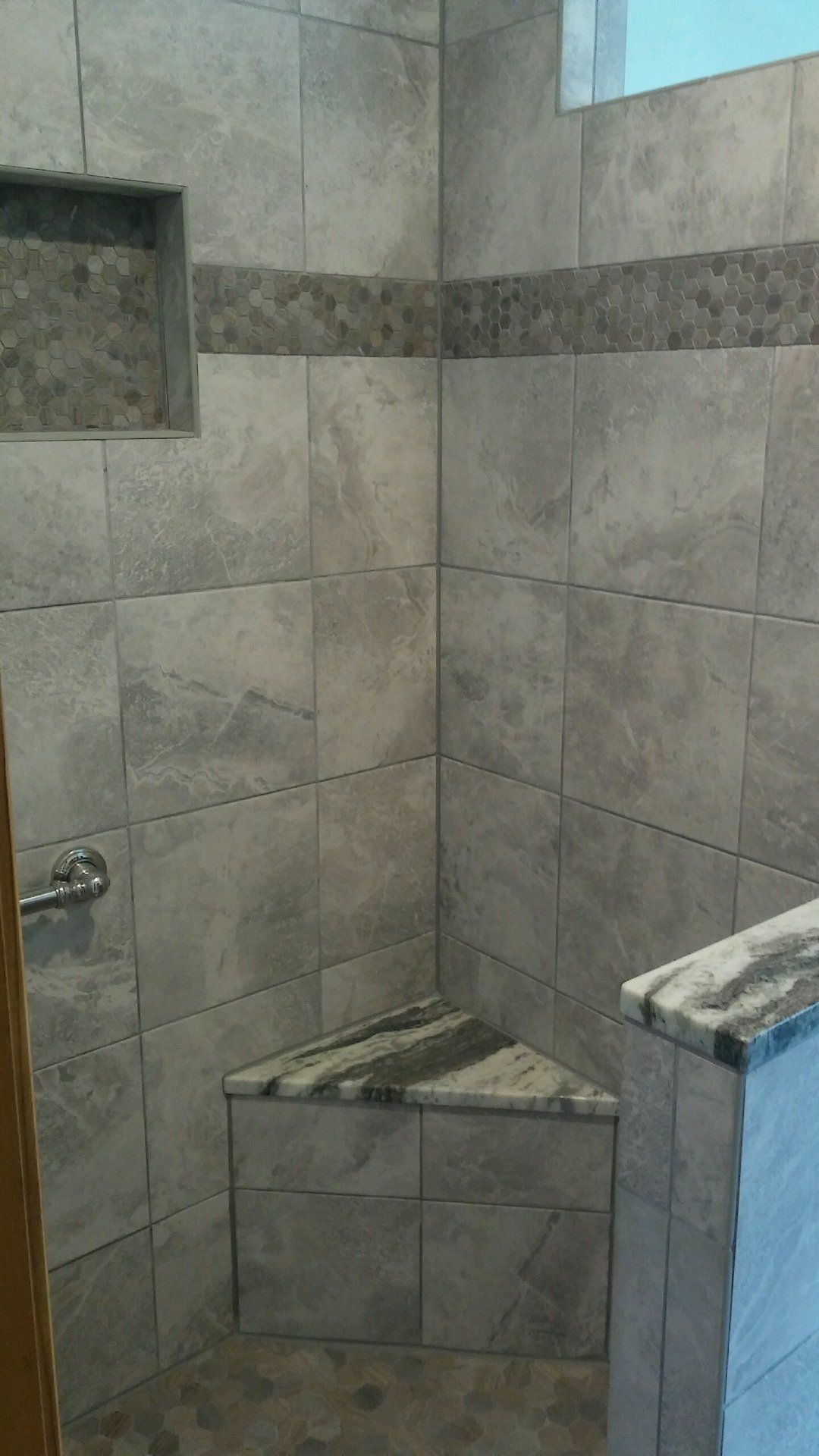 A bathroom with tiled walls and a corner shower seat.