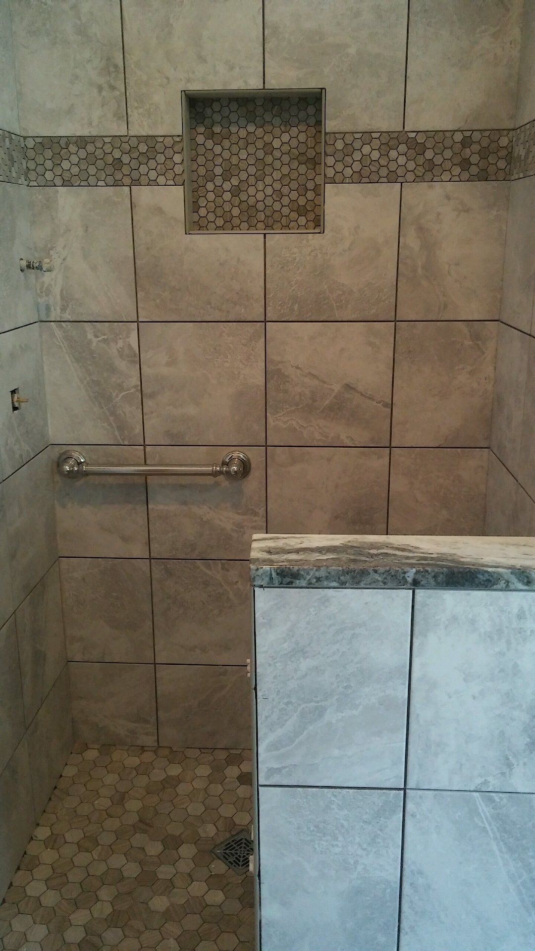 A walk in shower with tiled walls and a hand rail.