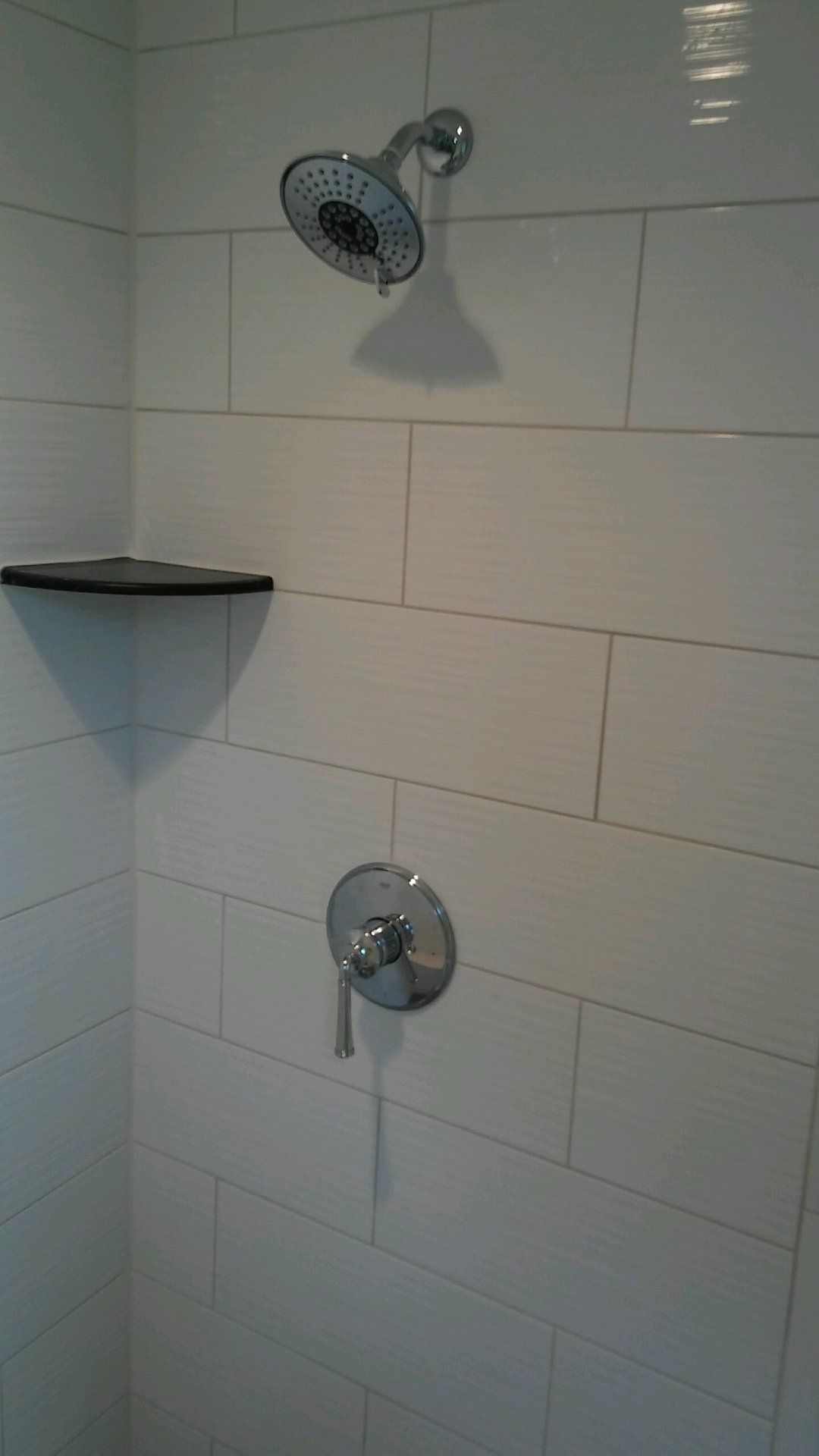 A shower with a shower head and a shelf on the wall.