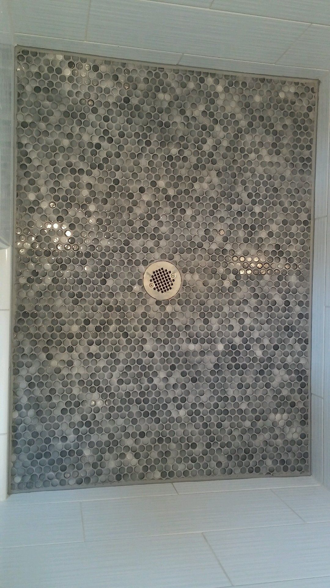A shower stall with a mosaic tile floor and a drain.