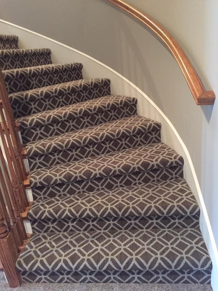 A set of curved stairs with a patterned carpet and a wooden railing.