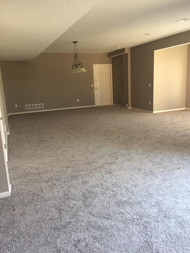 An empty living room with a gray carpet and a chandelier hanging from the ceiling.