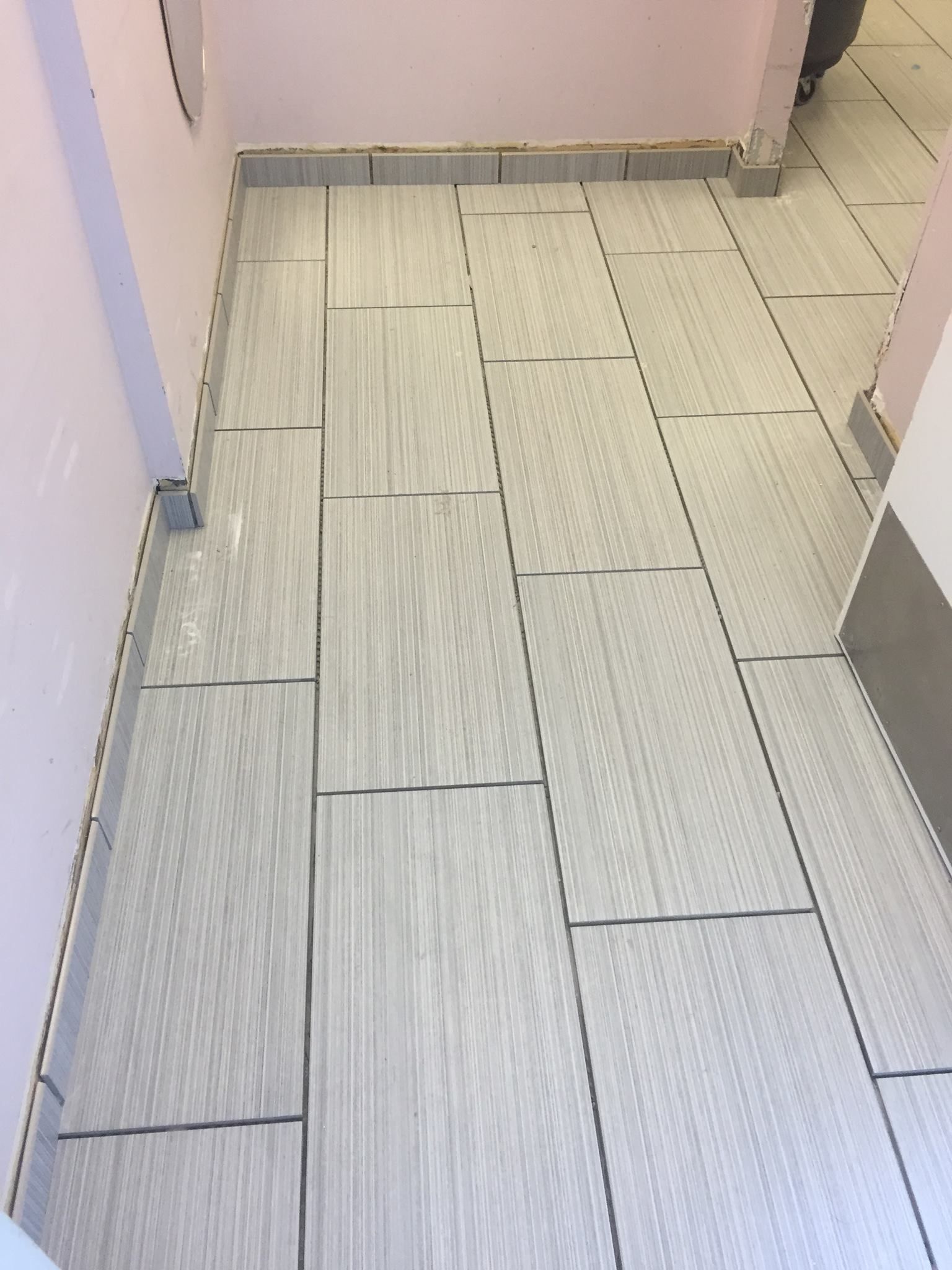 A white tile floor is being installed in a bathroom.