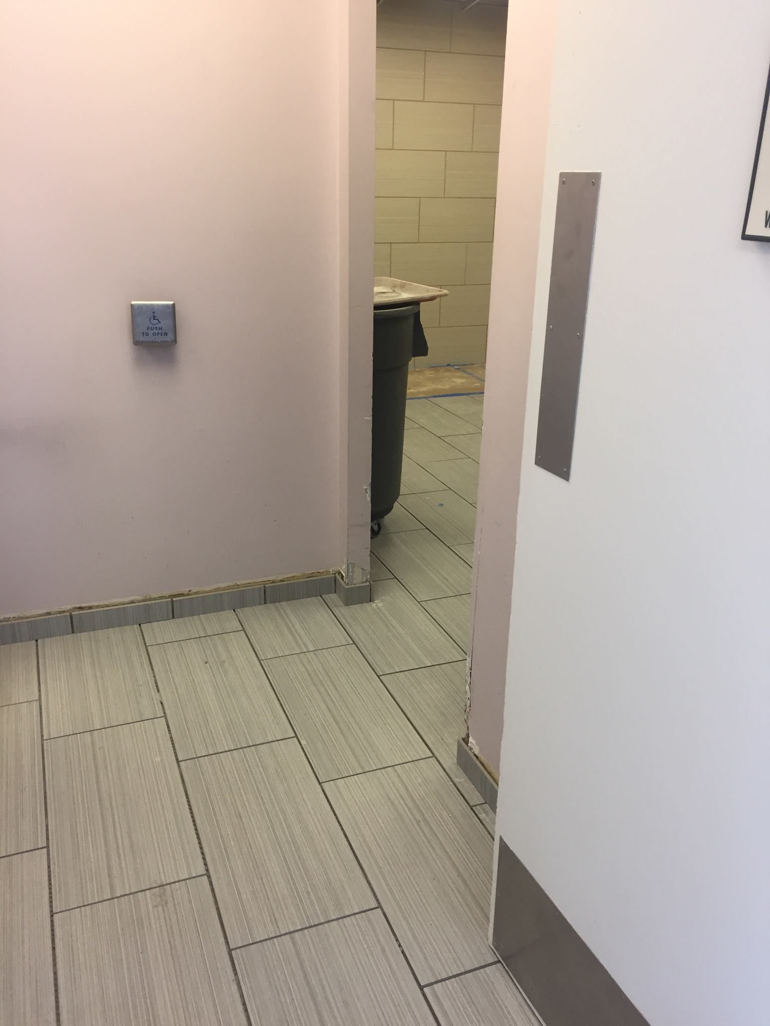 A hallway with tile floors and a trash can in the corner.
