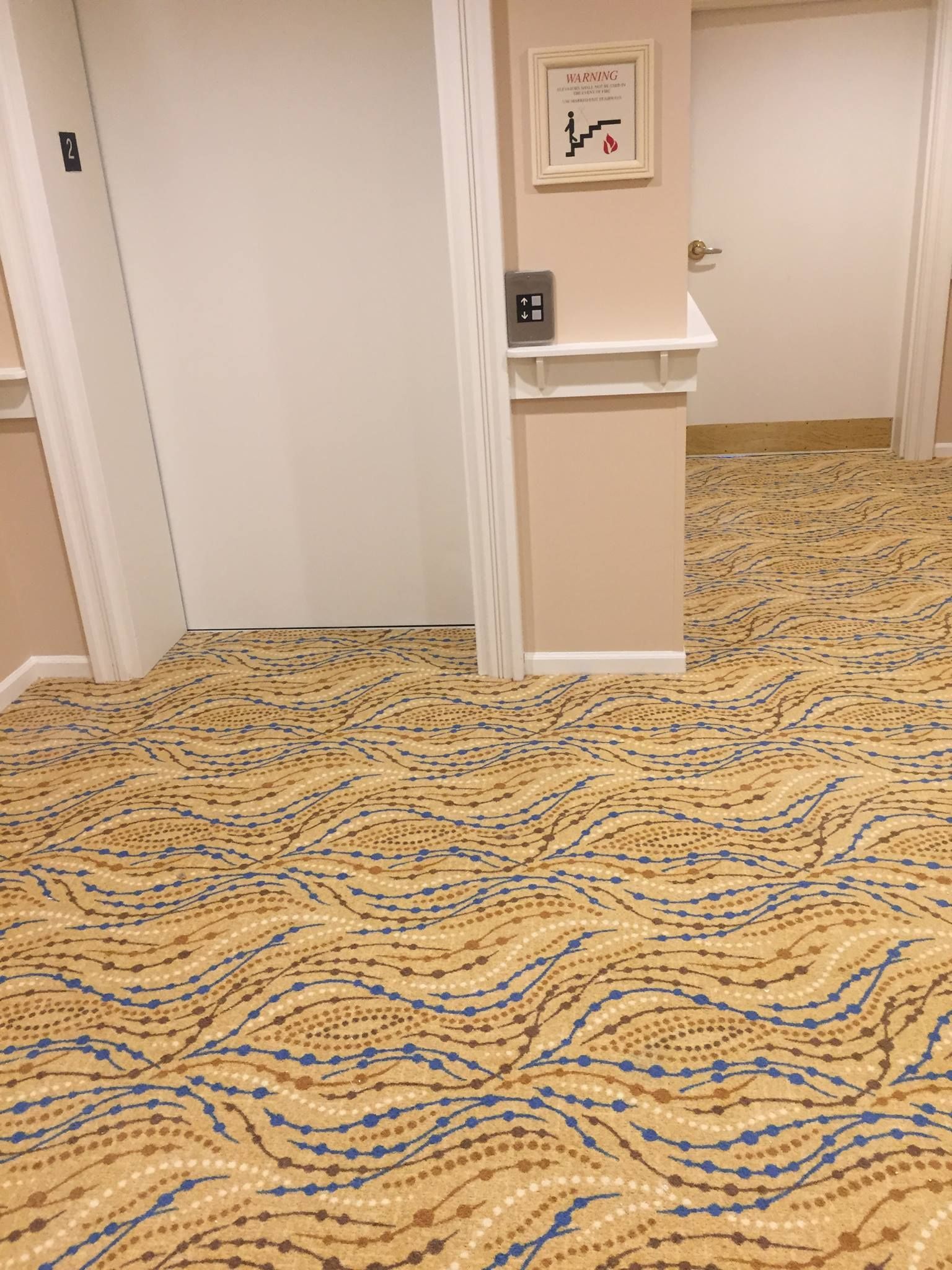 A hallway with a carpeted floor and a picture on the wall.