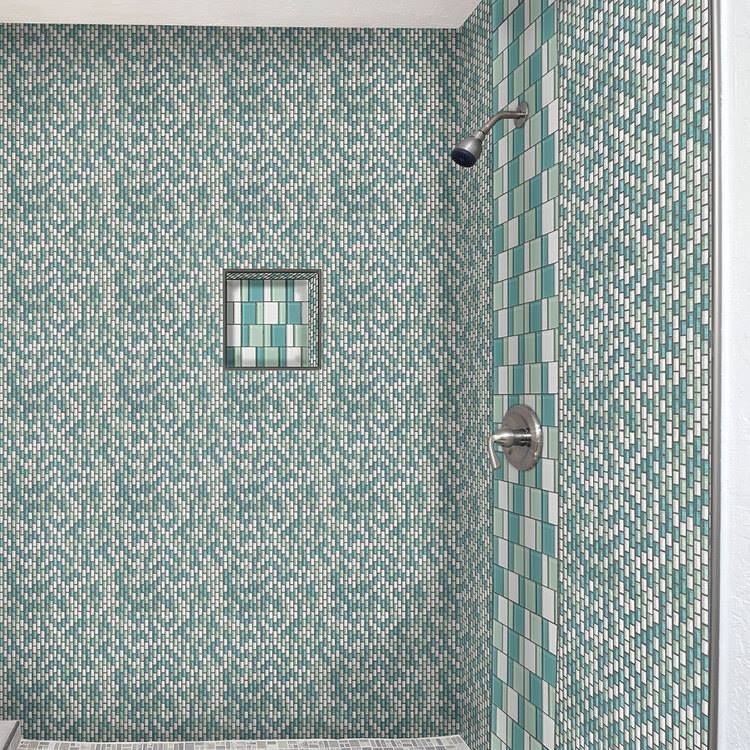 A shower with green and white tiles and a shower head.