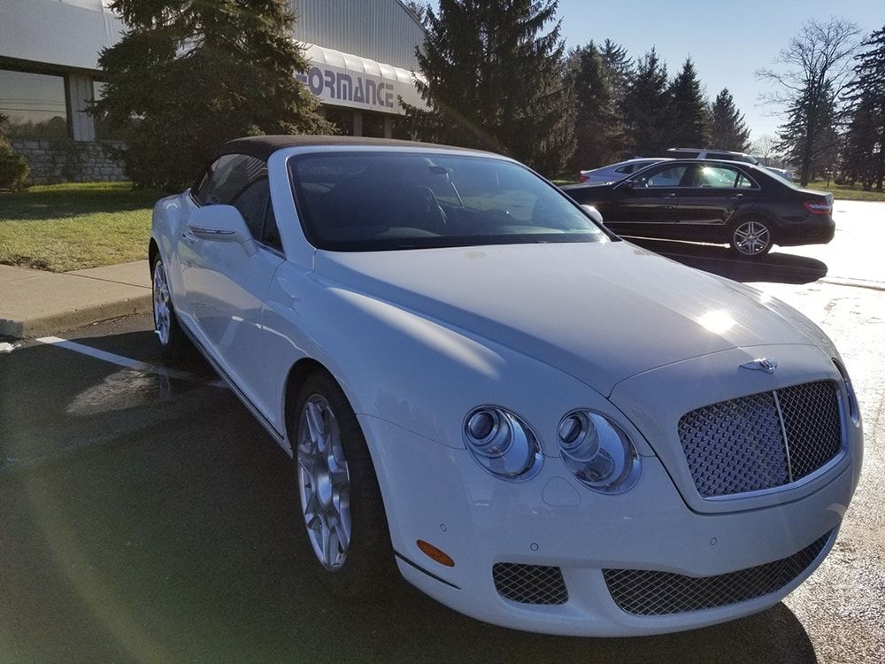 A white bentley convertible is parked in a parking lot