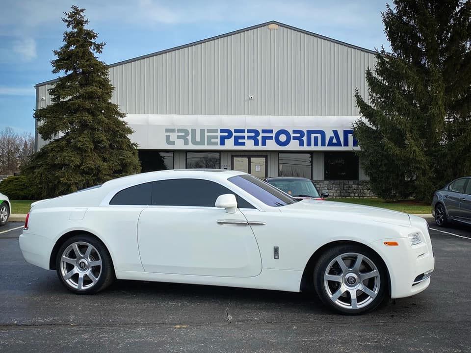 A white car is parked in front of a building that says true performance.