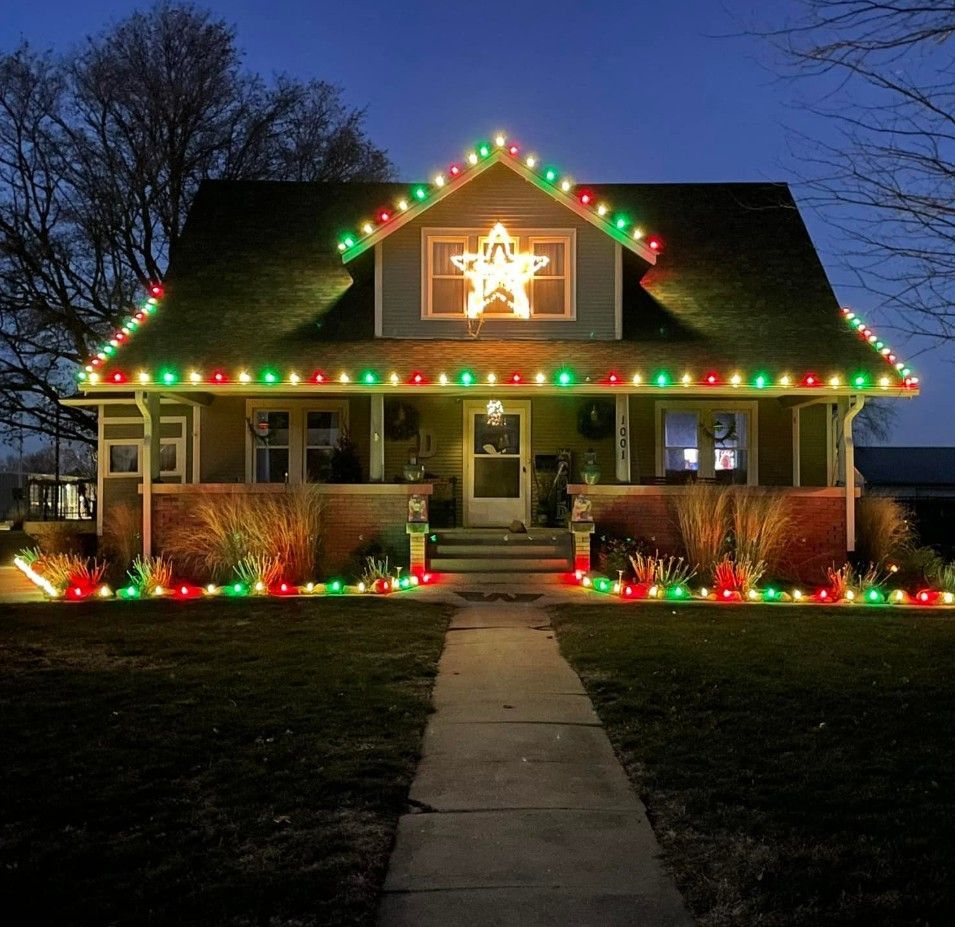 A house at twilight decorated for the holidays with glowing red and green lights and a bright star in the dormer window.