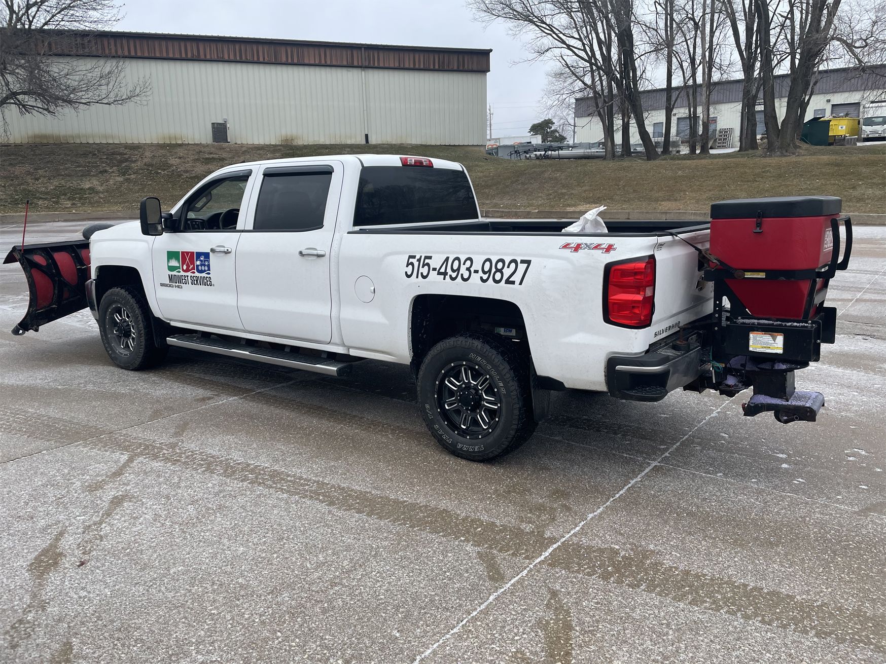 White pickup truck with plow and red salt spreader parked on a wet lot