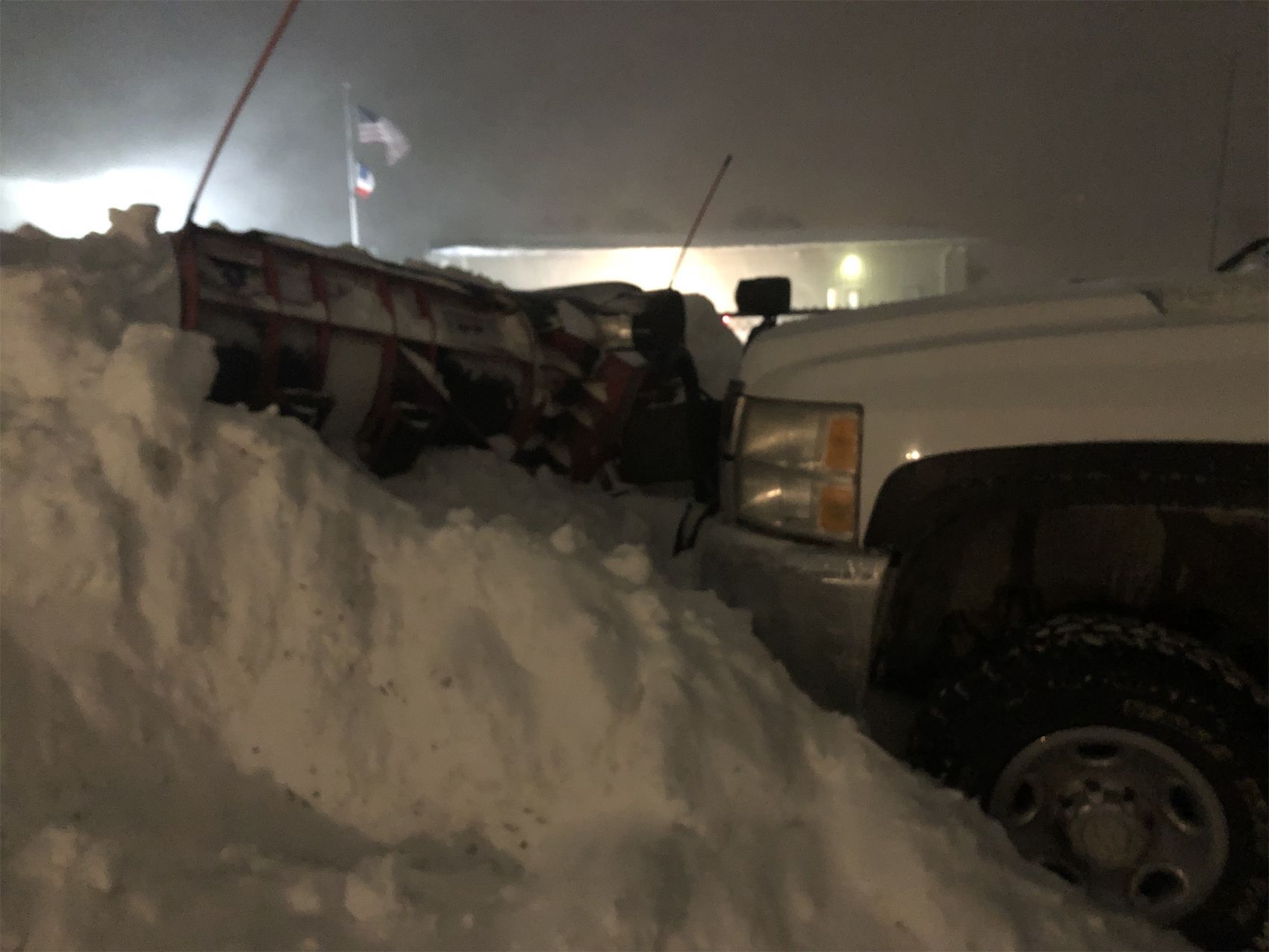 Snow-covered truck buried in a large snowbank at night, with another vehicle beside it.