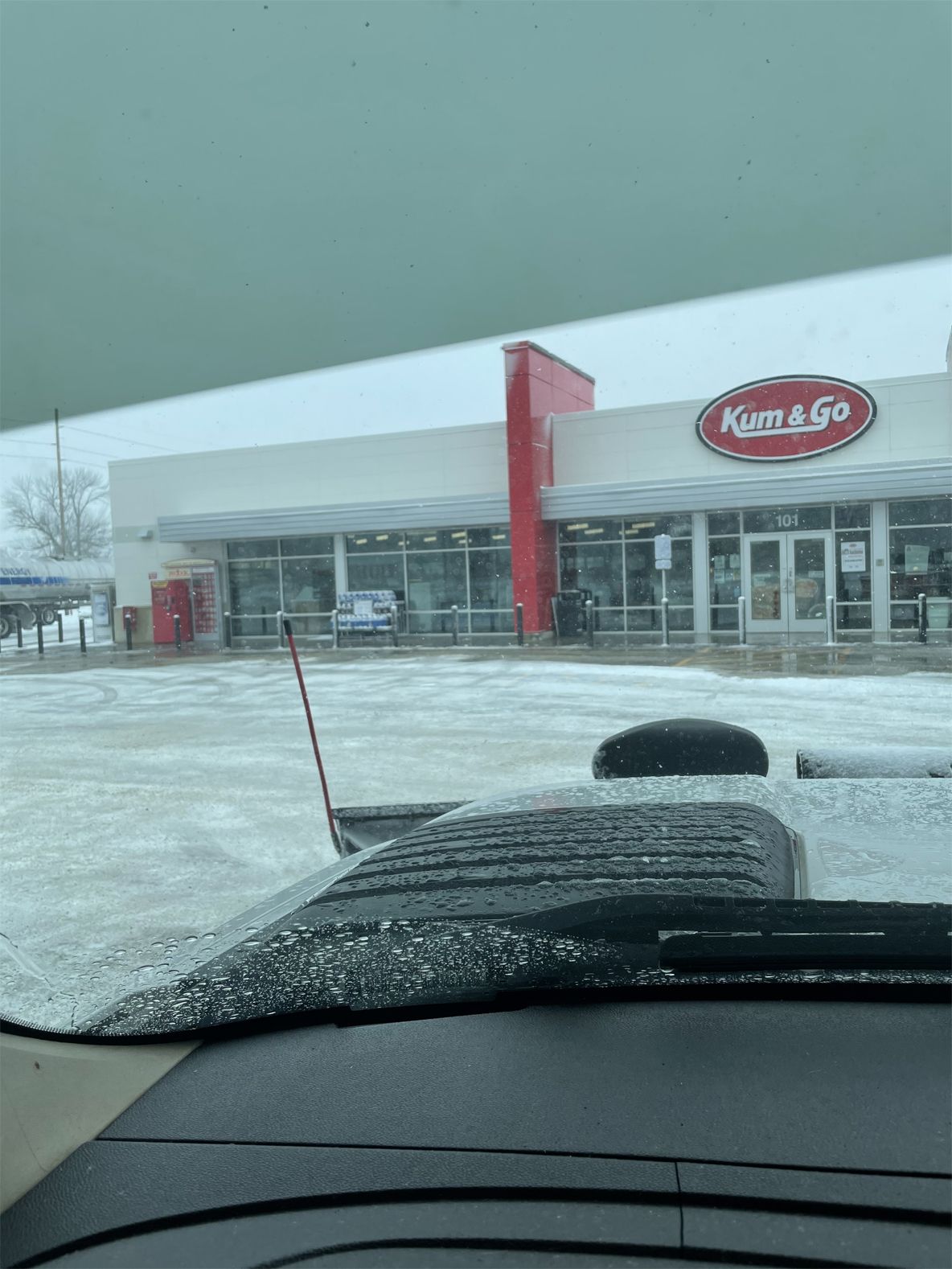Snow-covered gas station seen through a car windshield in winter.