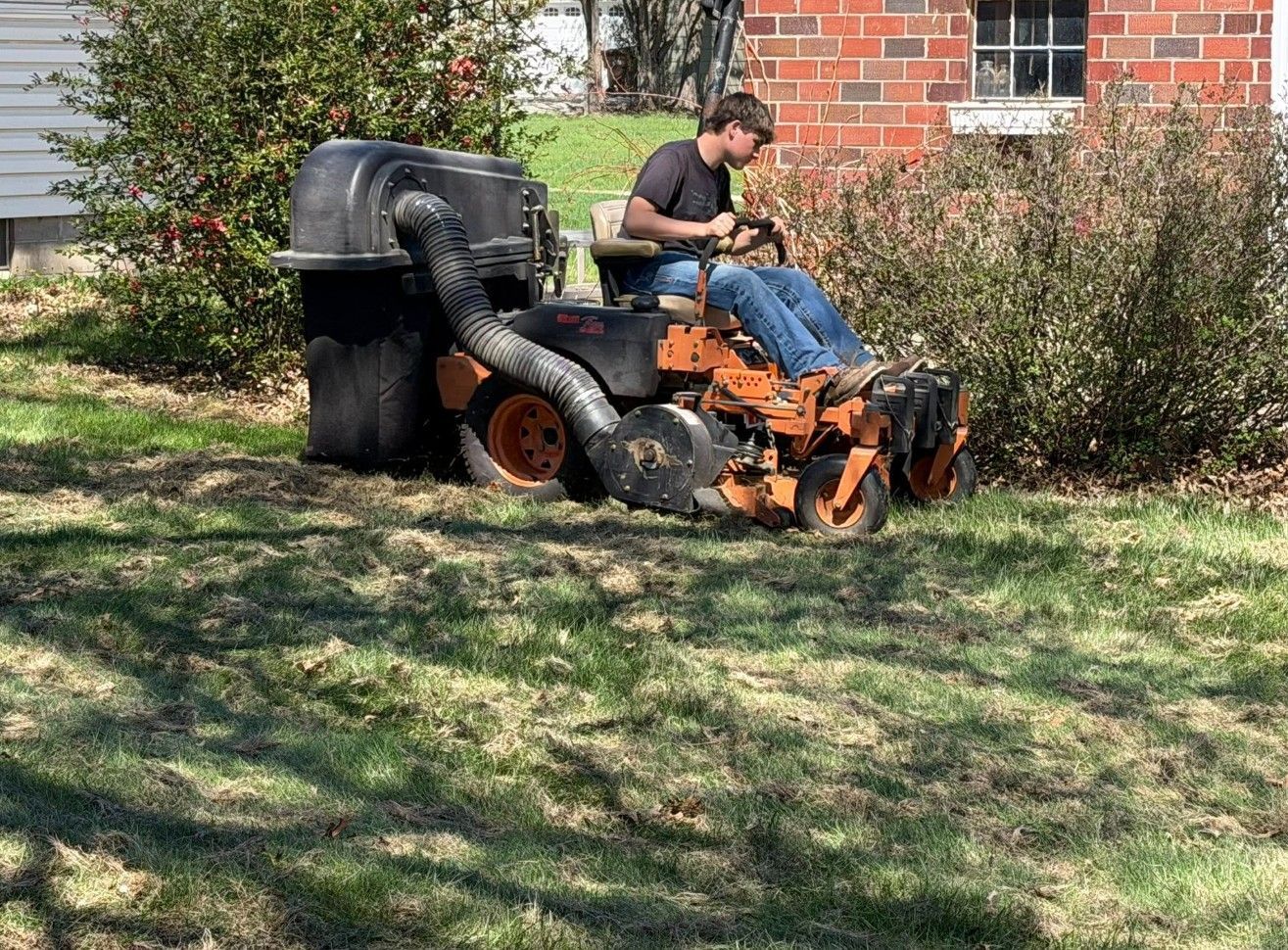 Man on orange lawn mower mowing grass beside a brick house and bushes