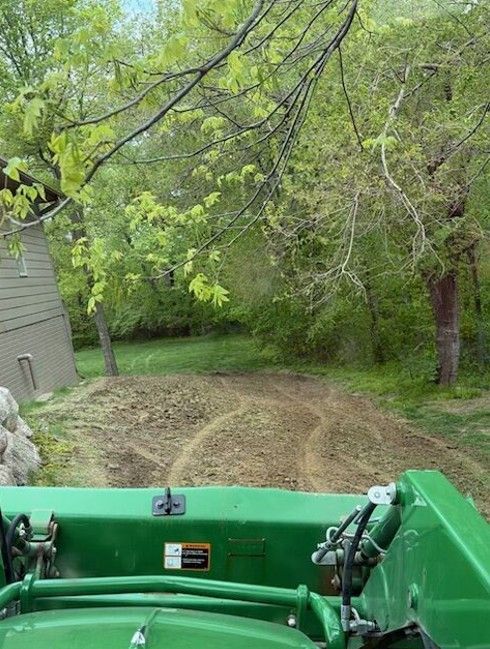 Green tractor front view driving along a mown grassy path beside trees and a house