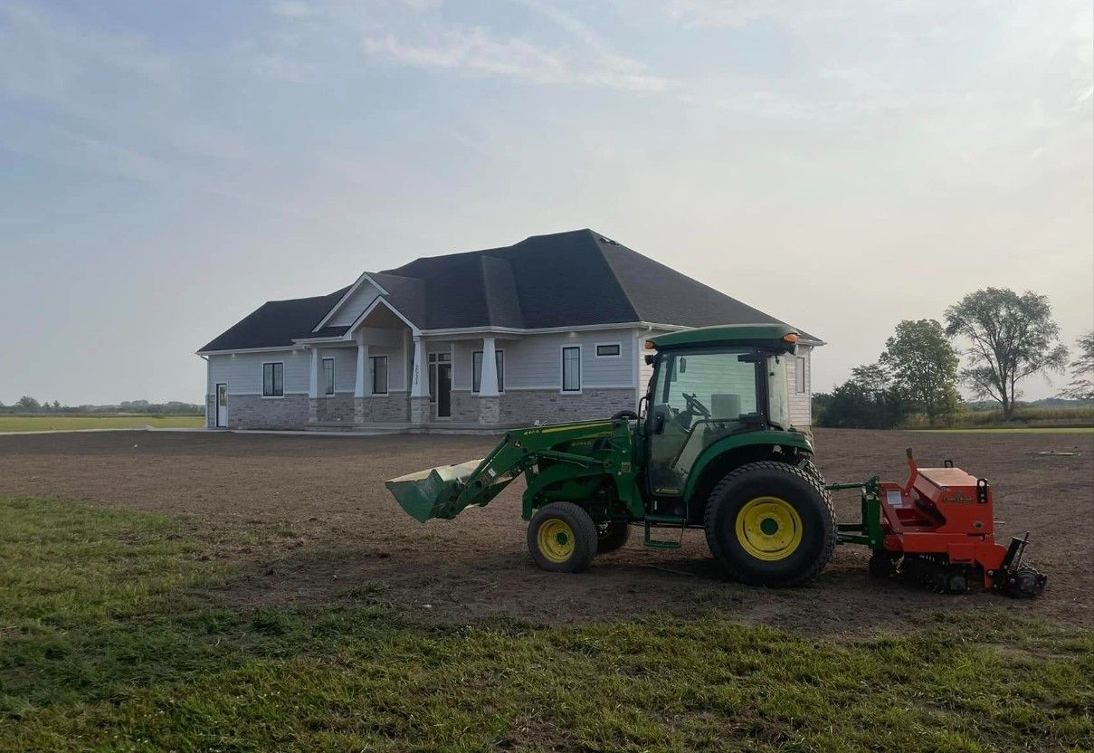 A John Deere tractor with a seeding attachment in front of a new house, preparing the lawn.