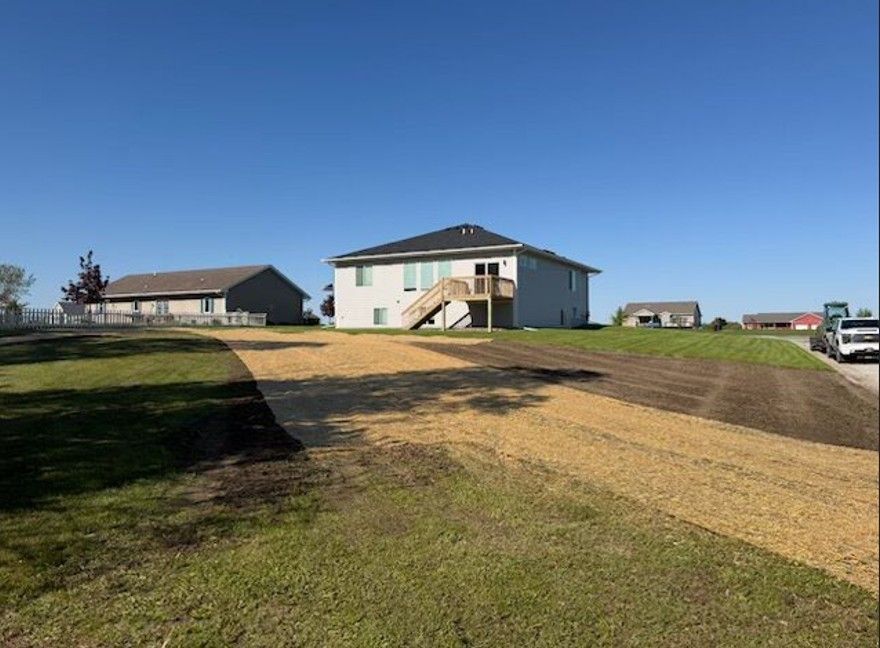 Suburban house on a grassy lot with a dirt driveway under a clear blue sky