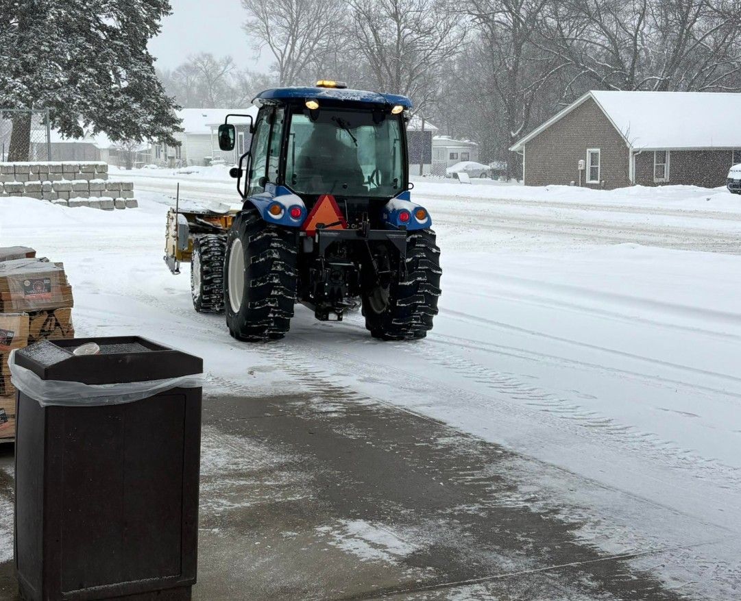 Blue tractor clearing snow on a street in a wintery residential area.