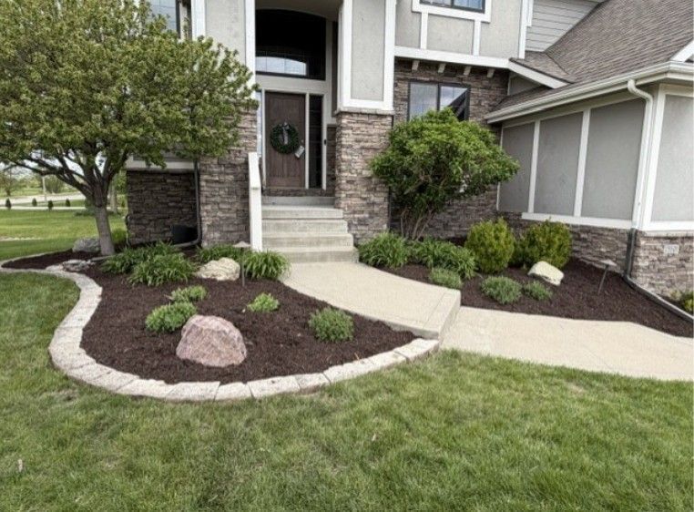 Front yard landscaping with stone edging, mulch beds, shrubs, and a curved concrete walkway to the front door.