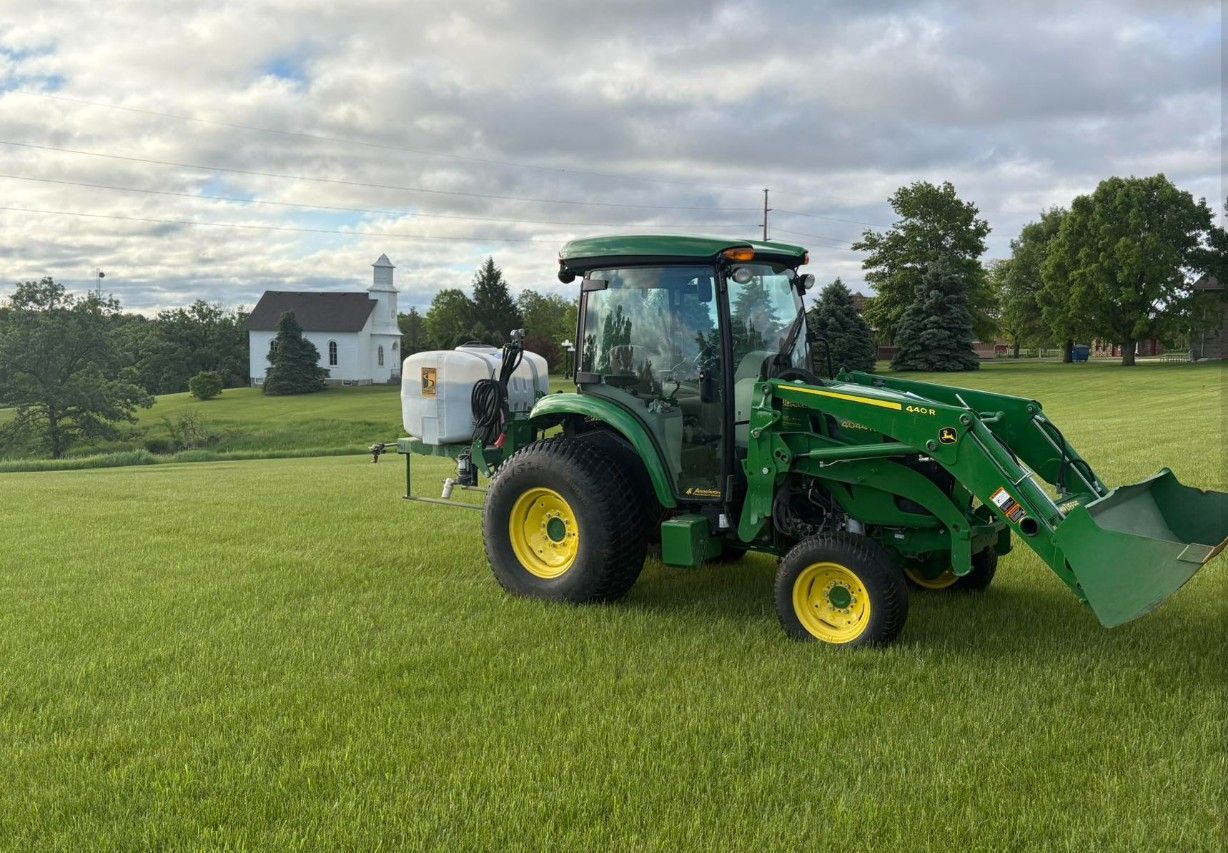 Green tractor with front loader on a grassy field under a cloudy sky.