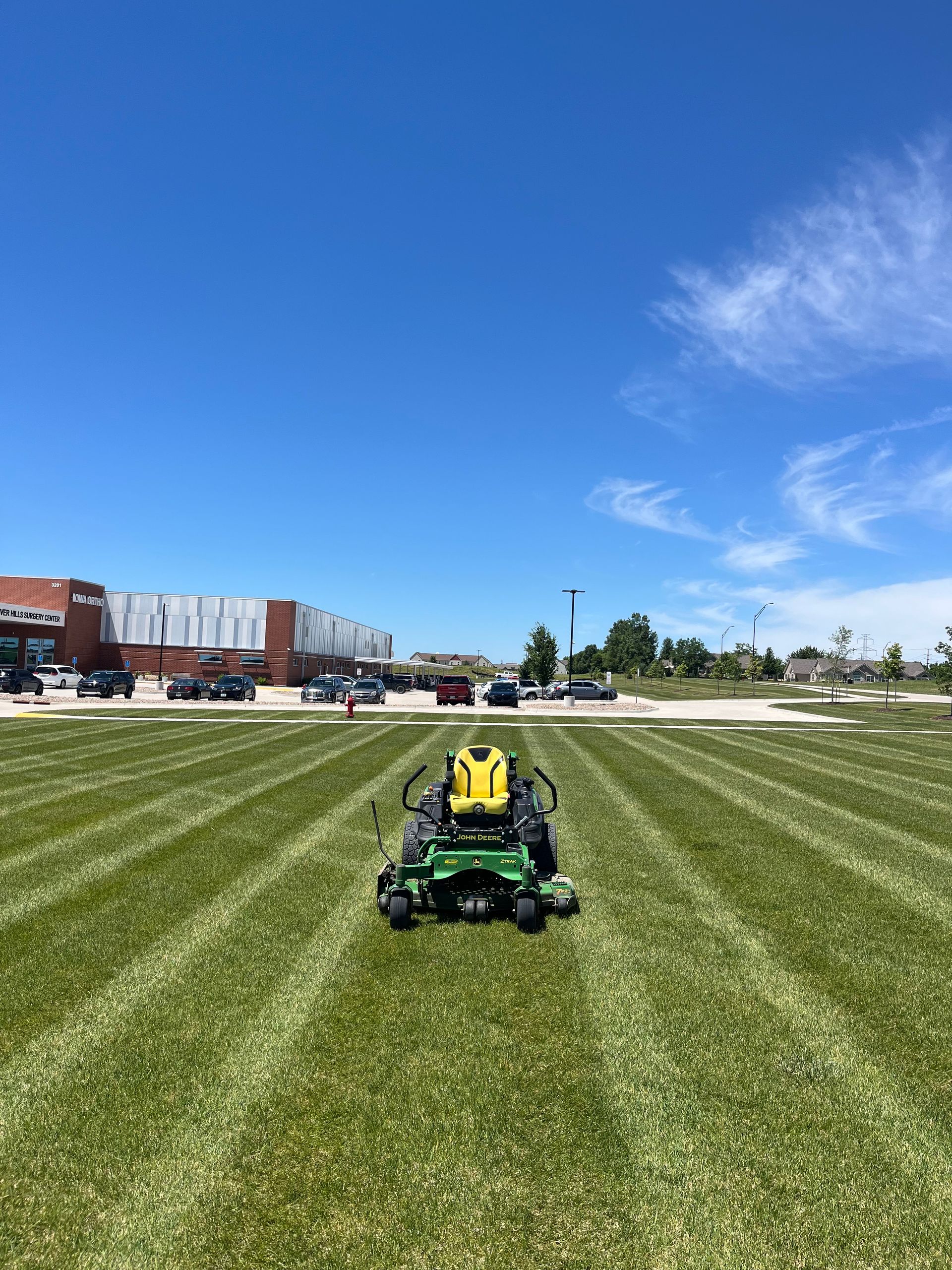 Person on green riding mower on striped grass field under a blue sky.