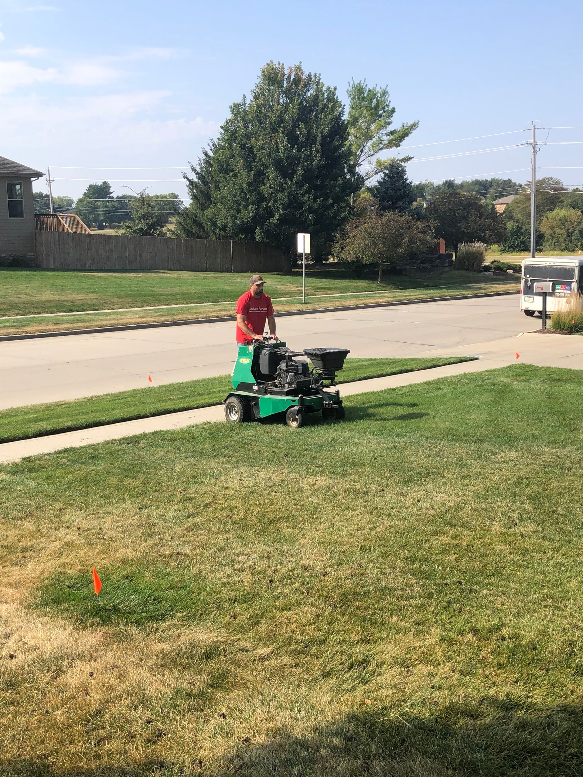 Person mowing a grassy roadside lawn with a green riding mower on a sunny day