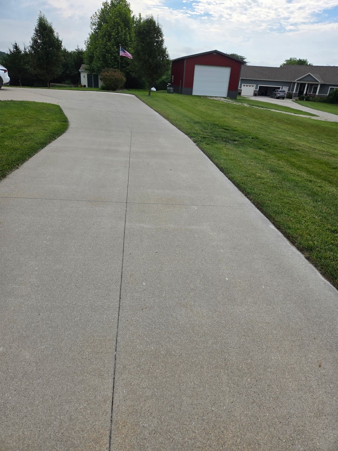 Curving concrete driveway beside green lawns leading to a red garage and suburban homes