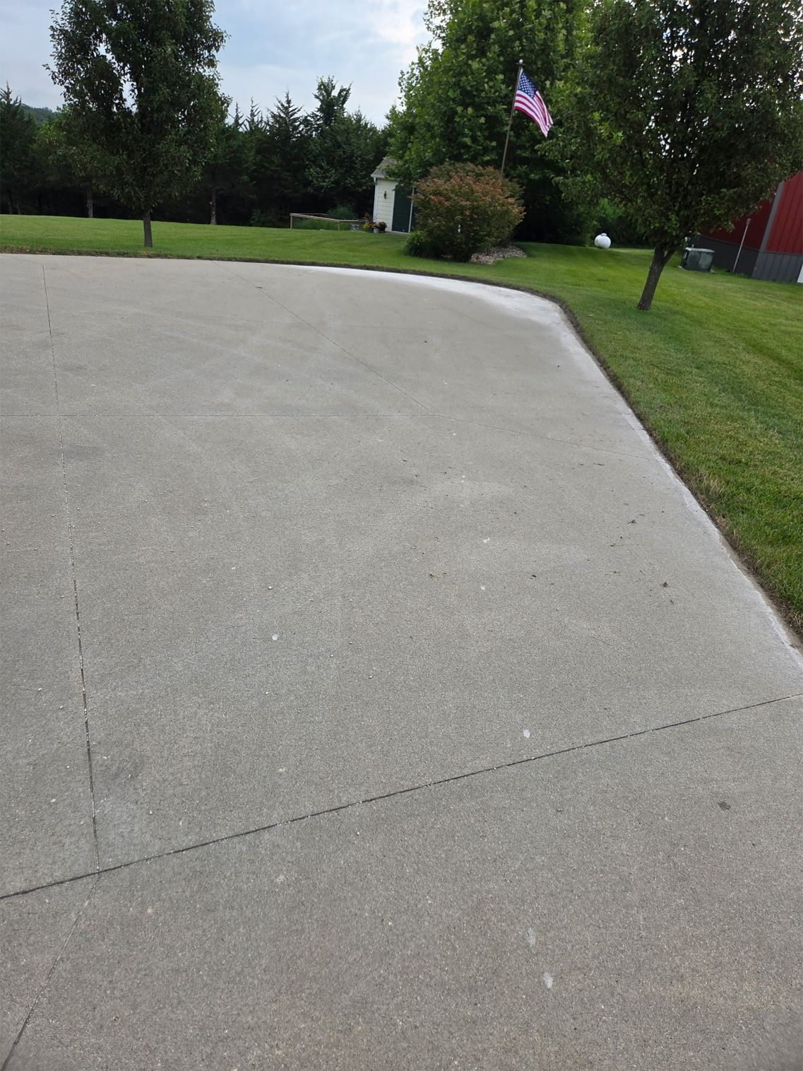 Driveway beside a grassy lawn and trees, with an American flag in the background.