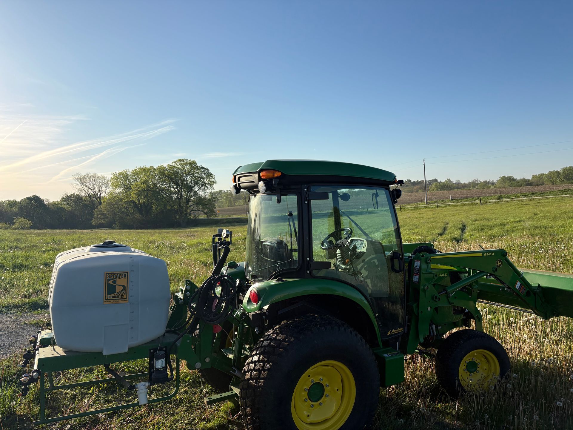 Green tractor with front loader and sprayer in a field under a clear blue sky