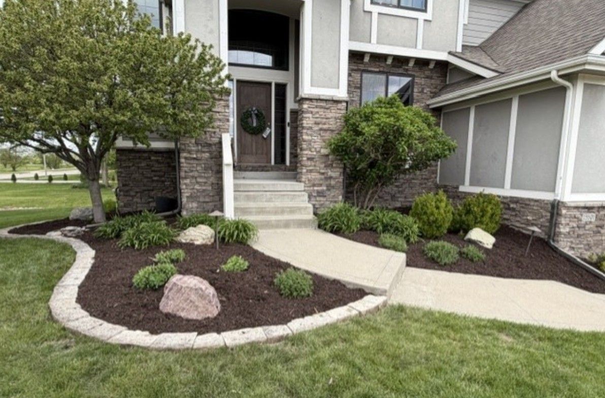 Front entry walkway with curved concrete paths, stone steps, and landscaped shrubs in front of a house