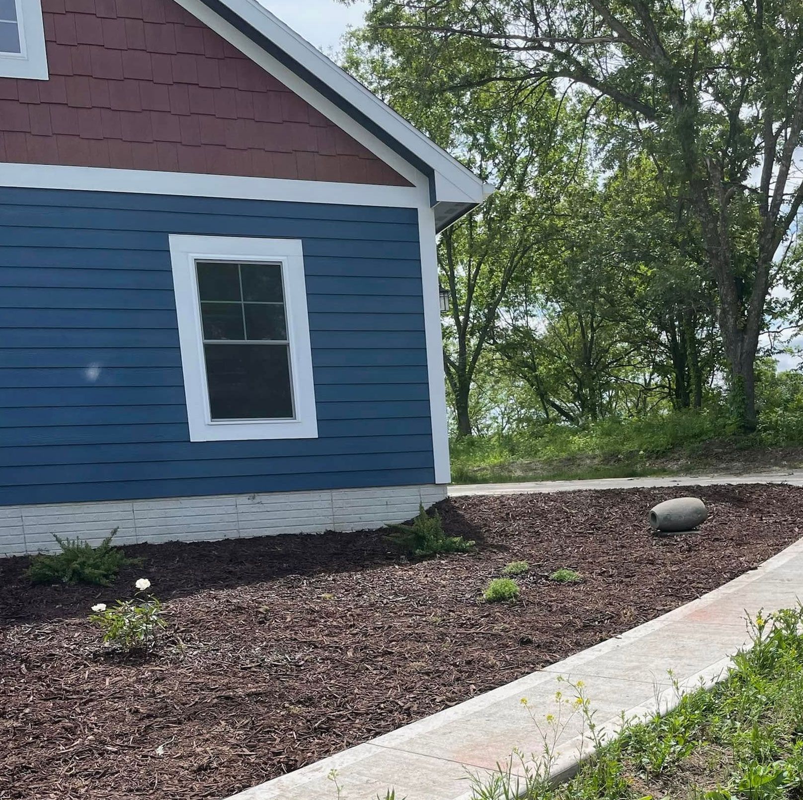 Blue house siding with white trim beside a mulched garden bed and curved concrete path.