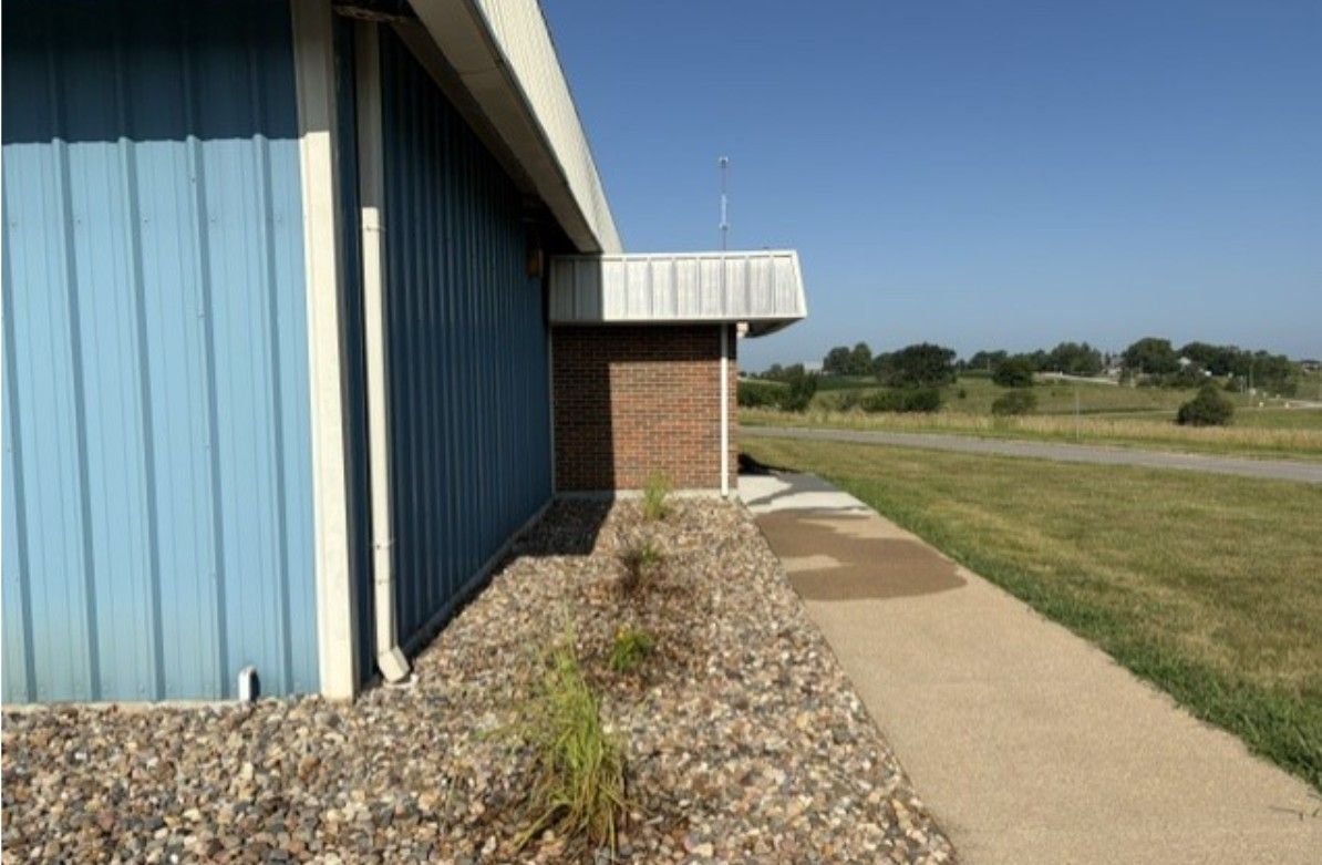 Blue building beside gravel path and grass field under a clear sky.