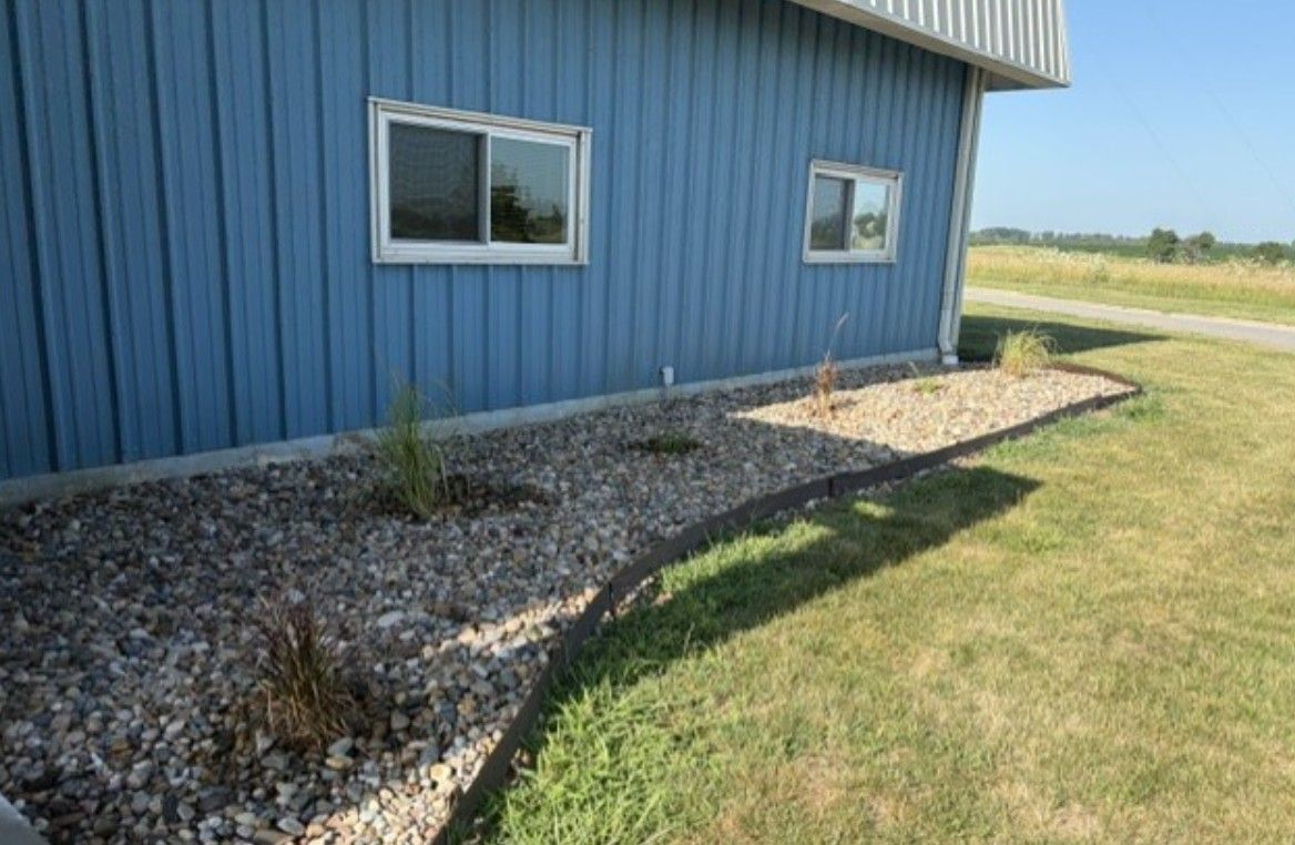Blue building exterior with two windows, gravel landscaping, and a grassy lawn under bright daylight.