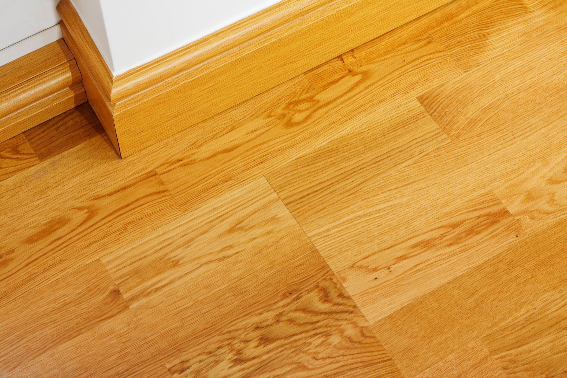Close-up of golden-brown wood flooring with a white baseboard and a corner of a white wall.