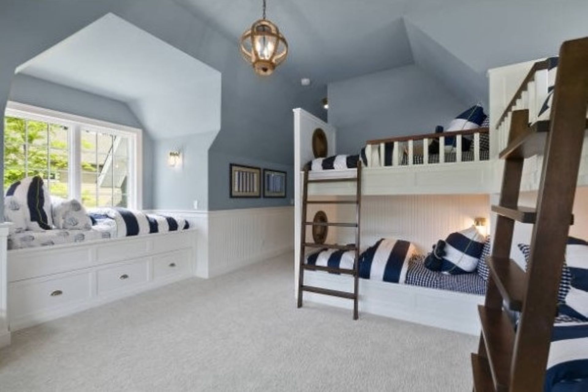 A nautical-themed bedroom with bunk beds, a window seat, and light blue walls.