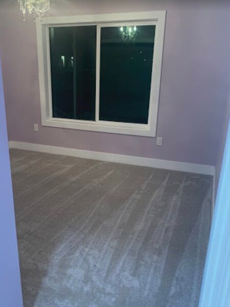 Empty room with lavender walls, gray carpet, and a large window.
