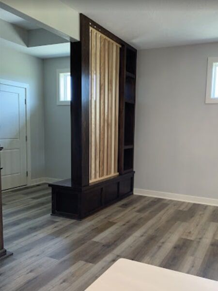 Dark wood room divider with built-in shelves and bench against light gray walls and wood-look flooring.