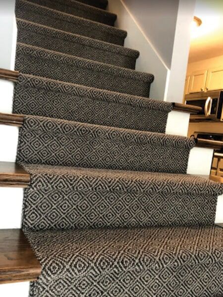 Carpeted staircase with dark gray diamond pattern, brown wood, and white trim.
