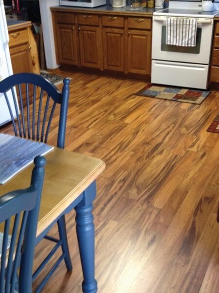 Wooden kitchen with wood cabinets, white stove, and blue chair at a table with a yellow tabletop.