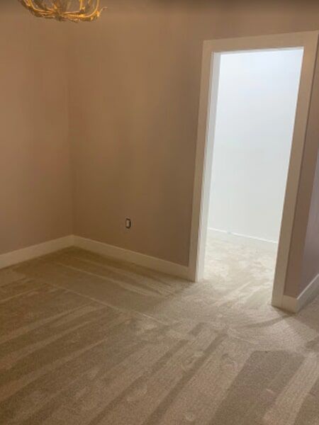 Empty room with light pink walls, white trim, beige carpet, and doorway to another room.