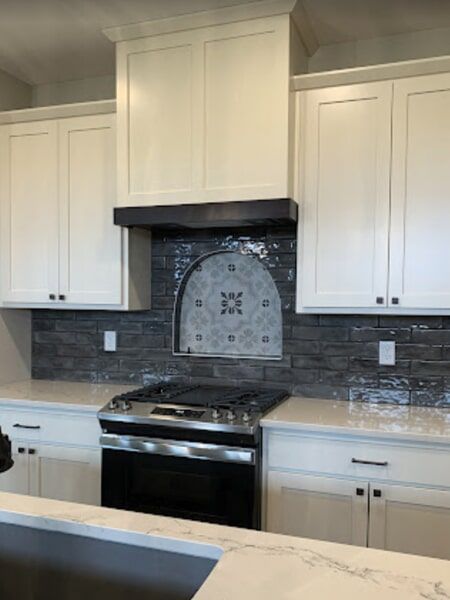White kitchen with stove, dark backsplash, and gray and white tile focal point.