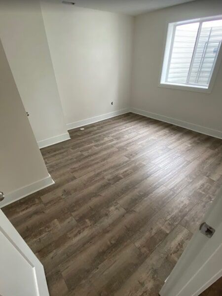 Empty room with wood-look flooring, white walls, and a window with blinds.