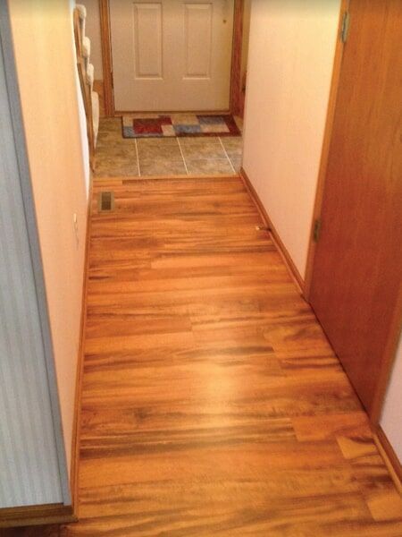 Wooden hallway with door at the end, leading to a front door with a rug.
