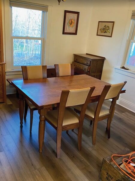 Dining room with wood table and six cream-colored chairs; window, dresser, and artwork in background.
