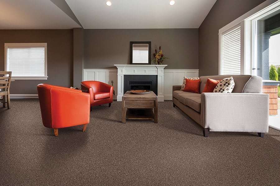 Cozy living room with brown carpet, fireplace, two orange chairs, and a gray sofa.