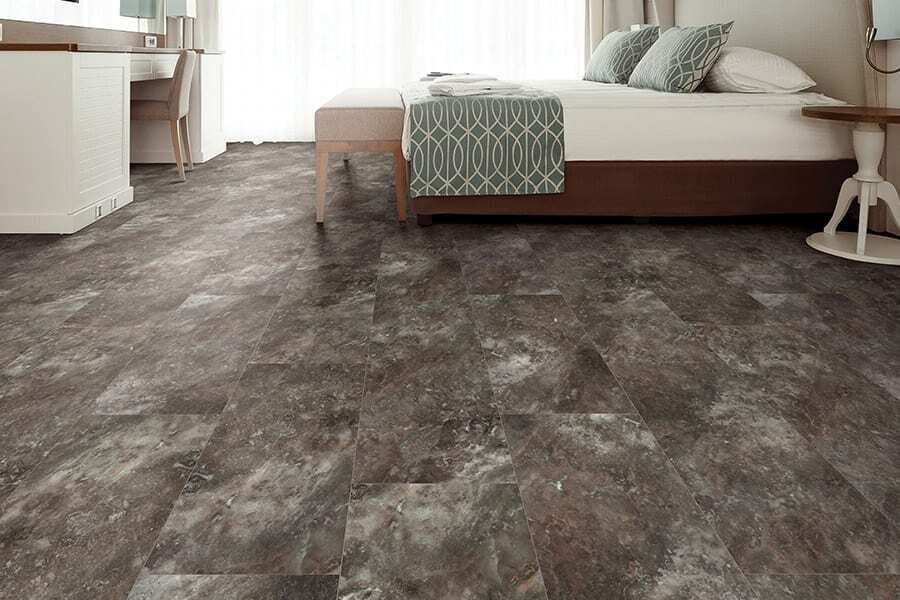 Bedroom with brown and gray flooring, white bed, side table, and desk.