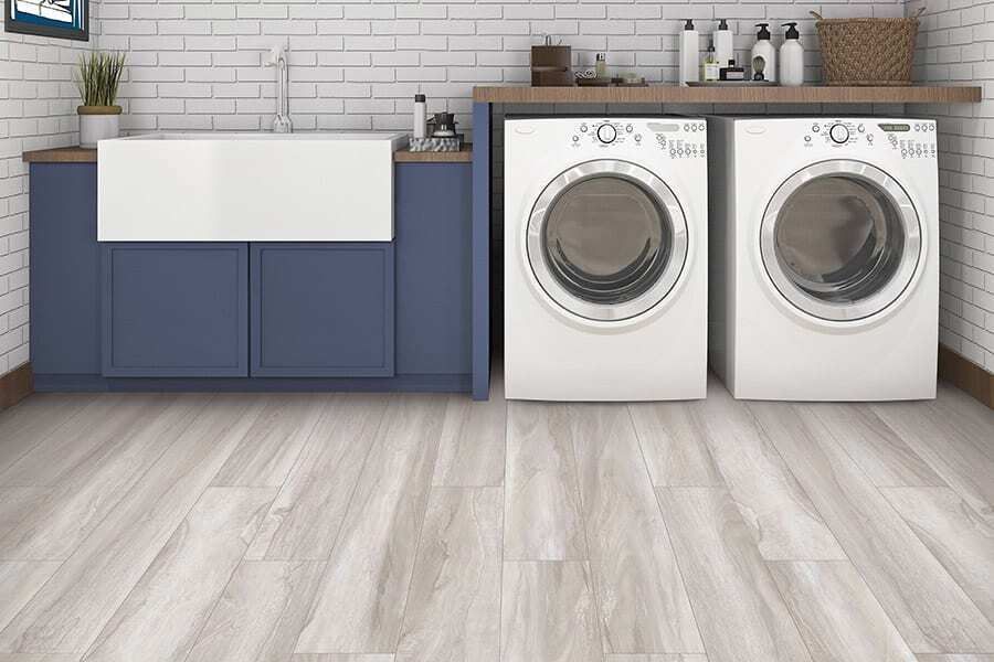 Laundry room with blue cabinets, white brick wall, and light wood-look floor. Two white washers/dryers.