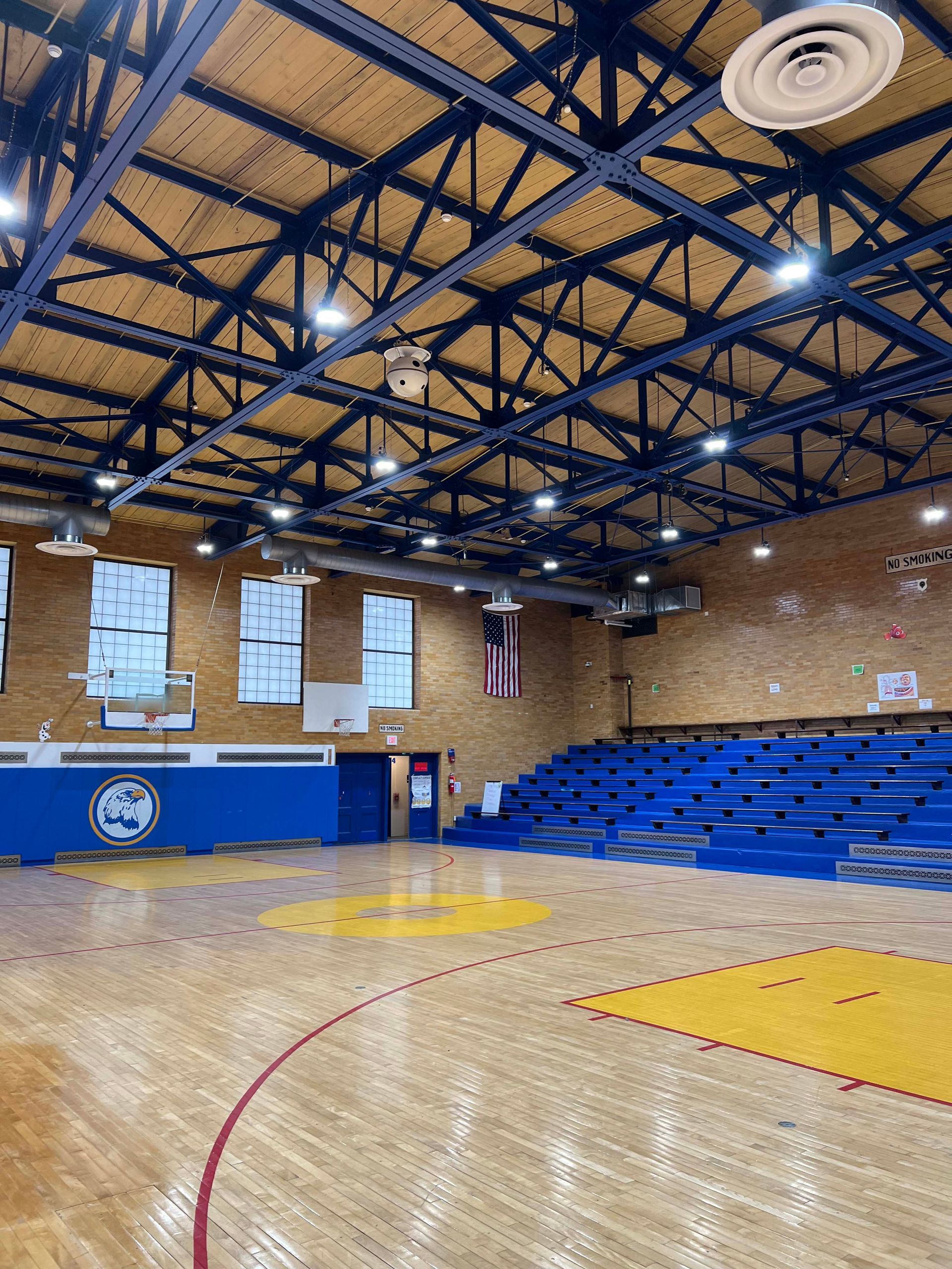 Empty gymnasium with blue bleachers, brick walls, and bright lights over a polished wood court